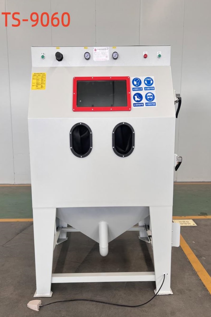 "TS-9060 model sandblasting machine with a large viewing window, user-friendly controls, and dust extraction system. Ideal for precise surface preparation in industrial applications. Features clear safety labels, a foot pedal for operation, and ergonomic hand gloves for safe and efficient blasting."
